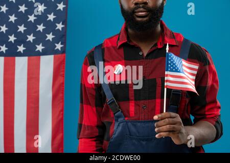 Junger bärtiger afroamerikanischer Ingenieur in Arbeitskleidung, der uns Flagge hält Stockfoto