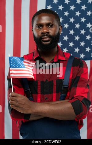 Junger bärtiger afroamerikanischer Arbeiter in Flanell und Overalls, die uns halten Alarmmeldung Stockfoto