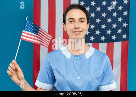 Glücklich junge Brünette Zimmermädchen in blau Uniform hält kleine Amerikaner Alarmmeldung Stockfoto