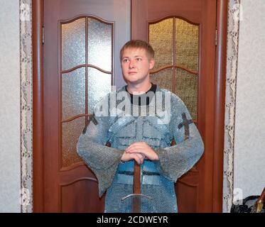 Ein Mann, gekleidet in ein ritterliches Kettenhemd zu Hause in seinem Zimmer. Knight's Schwert in den Händen eines Mannes. Stockfoto