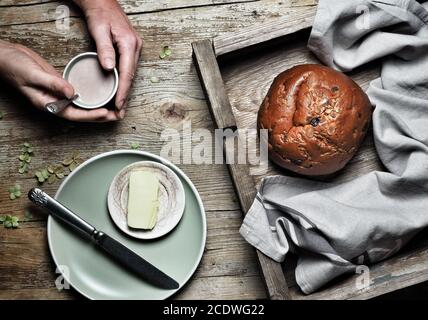 Süßes Brot, typisch slowakischer Kuchen. Eine Tasse Kakaommilch in der Hand der Frau und ein Stück Butter auf dem Teller auf vintage Holzhintergrund. Overhead-Aufnahme. Stockfoto