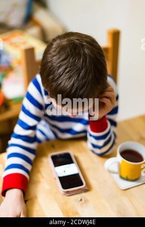 Kleiner Junge spielt Koch mit Smartphone und Kaffee in Die Tasse Stockfoto