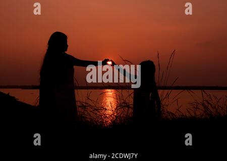 Am 5. Januar 2020 orange Silhouette Sonnenuntergang von Mutter und Tochter, die Liebe Zeichen bei bacreswar Damm, birbhum, West Bengalen, Indien Stockfoto