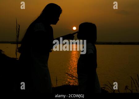 Am 5. Januar 2020 orange grüne Silhouette der Mutter und der Tochter bei Sonnenuntergang bakswar Damm, birbhum, Westbengalen, Indien Stockfoto