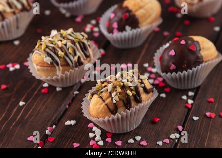 Nahaufnahme hausgemachte Kekse geformte Nüsse mit Sahne, Schokolade Glasur auf Holztisch als Hintergrund, rot, rosa und weißen Zucker streuen Herzen, decorati Stockfoto