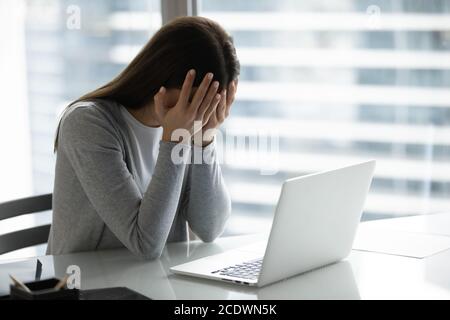 Frustrierte überarbeitete Geschäftsfrau, die das Gesicht mit den Händen bedeckte und am Schreibtisch saß Stockfoto