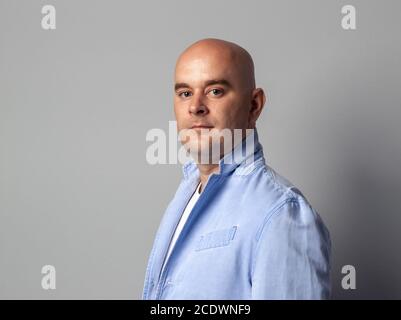 Glatzköpfige Mann in einer blauen Jacke gegen eine graue Wand Stockfoto