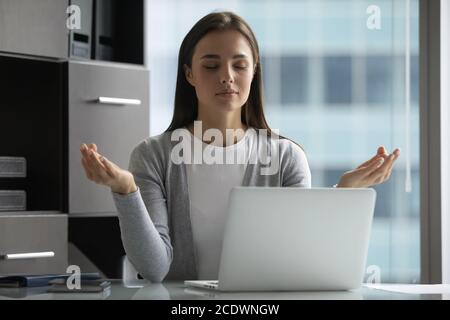 Friedliche junge Geschäftsfrau mit geschlossenen Augen meditiert am Arbeitsplatz Stockfoto