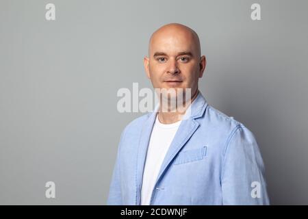 Glatzköpfige Mann in einer blauen Jacke gegen eine graue Wand Stockfoto