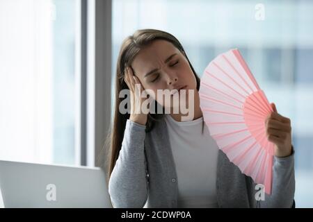 Überhitzte unglückliche junge Geschäftsfrau winkt Papierventilator im Büro Stockfoto