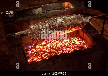 Gegrilltes Fleisch in Folie auf offenem Feuer. Ganzkörper Tier mit Folie auf einem großen Grill, Restaurant Küche gewickelt. Stockfoto