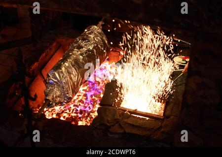 Gegrilltes Fleisch in Folie auf offenem Feuer. Ganzkörper Tier mit Folie auf einem großen Grill verpackt, Restaurant Küche in Aktion Stockfoto