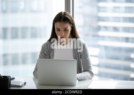 Fokussierte junge Frau, die im modernen Büro am Laptop arbeitet Stockfoto