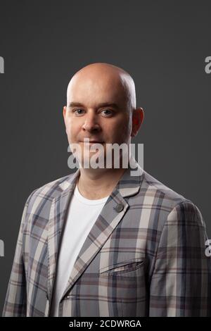 Cute glatzköpfige Mann in einer Jacke und T-Shirt zeigt gegen eine graue Wand Stockfoto
