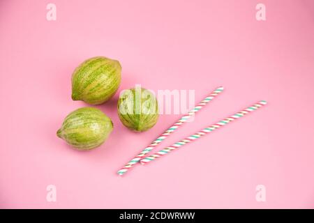 Gestreifte Zitronen und Papier Trinkhalme auf rosa Hintergrund. Pinkfarbene Eureka-Zitronen, zwei Cocktail-Trinkhalme Stockfoto