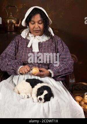 Reenactment-Szene eine schwarze viktorianische Maid Kartoffelschälen in eine antike Küche Stockfoto