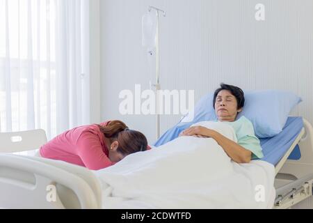 Eine ältere asiatische Frau ist krank und schläft im Bett neben ihrer Tochter schlief in der Pflege ihres Krankenhausbettes. Stockfoto