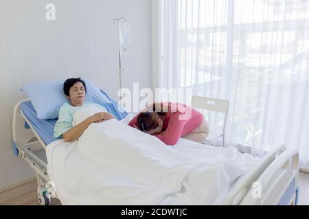 Eine ältere asiatische Frau ist krank und schläft im Bett neben ihrer Tochter schlief in der Pflege ihres Krankenhausbettes. Stockfoto