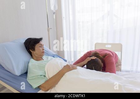 Eine kranke Mutter im Bett, eine asiatische Frau rieb sich den Kopf ihrer Tochter schlafend im Krankenhausbett Stockfoto