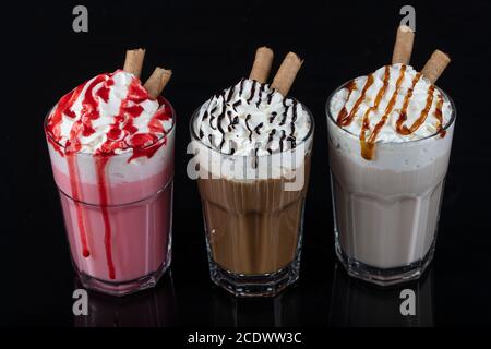 Drei Gläser bunte Milchshake Cocktails - Schokolade, Erdbeere und Vanille, isoliert auf schwarzem Hintergrund. Stockfoto