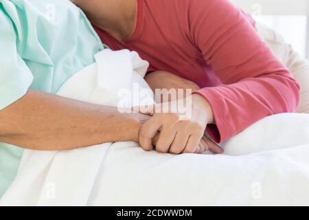 Hand in Hand mit einer kranken älteren Mutter, die darin liegt Ein Krankenhausbett mit Wärme und Pflege Stockfoto