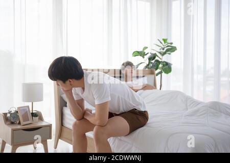 Ein schwuler Mann aus Asien, der nach einem Streit mit seinem Freund über die Idee eines LGBT-Paares im Bett sitzt. Stockfoto