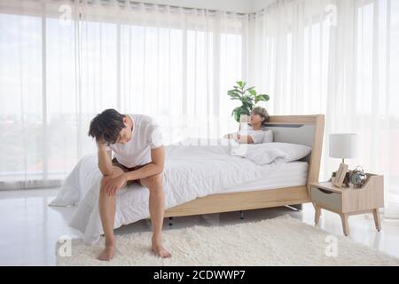 Ein schwuler Mann aus Asien, der nach einem Streit mit seinem Freund über die Idee eines LGBT-Paares im Bett sitzt. Stockfoto