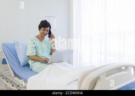 Die älteren asiatischen Frauen sitzen im Bett, erholen sich, sprechen am Telefon, und machen Besorgungen auf Laptops, in Krankenhäusern, Sonderzimmern. Stockfoto