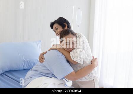 Eine junge asiatische Frau, die im Krankenhaus krank ist, umarmt ihre Mutter, die sich um sie kümmert. Stockfoto