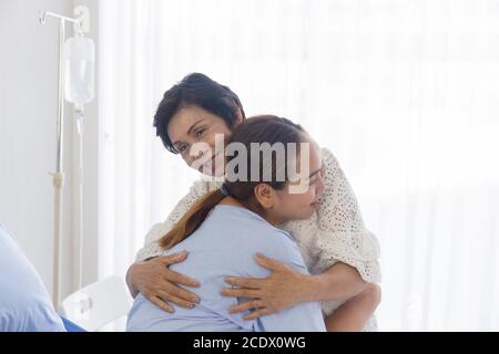 Eine junge asiatische Frau, die im Krankenhaus krank ist, umarmt ihre Mutter, die sich um sie kümmert. Stockfoto