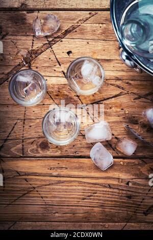 Wodka in den Schnapsgläsern auf dem hölzernen Hintergrund, vereißtes starkes Getränk im vernebelten Glas. Draufsicht Stockfoto