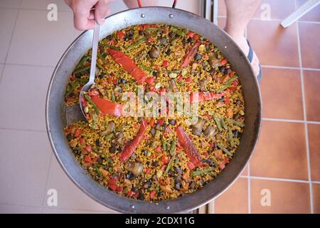 Traditionelle Paella aus Alicante (Valencia, Spanien): Paella mit magerem Fleisch und Gemüse. Nicht erkennbare Person, die Paella mit einem Löffel serviert. Stockfoto