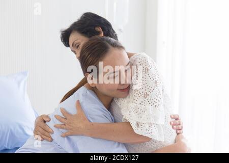 Eine junge asiatische Frau, die im Krankenhaus krank ist, umarmt ihre Mutter, die sich um sie kümmert. Stockfoto