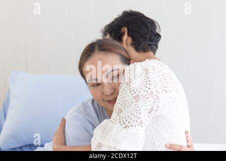 Eine junge asiatische Frau, die im Krankenhaus krank ist, umarmt ihre Mutter, die sich um sie kümmert. Stockfoto