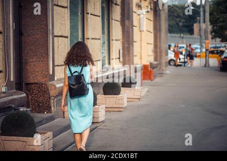 Rückansicht eines Hipster Mädchens in einem blauen Kleid Mit schwarzem Leder Rucksack zu Fuß auf der City Street Stockfoto