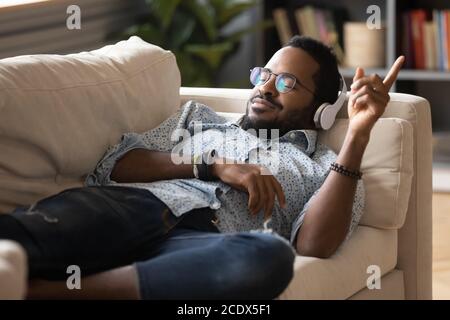 Zufriedener, positiver afroamerikanischer Mann, der auf der Couch liegt und Musik genießt Stockfoto