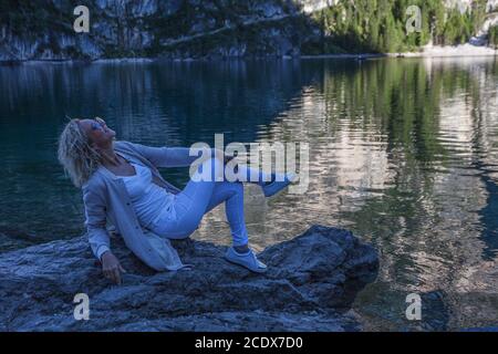 Blonde Frau posiert amüsiert vor dem kristallklaren Wasser des Sees, Prags See, Südtirol, Italien Stockfoto