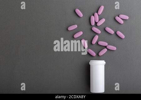 Ovale rosa Pillen werden aus einem Glas auf einem grauen Hintergrund gegossen. Leerzeichen für Text. Stockfoto