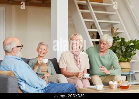 Glückliche ältere Leute sitzen auf dem Sofa, trinken Tee und erzählen Einander verschiedene Stockwerke im Zimmer Stockfoto