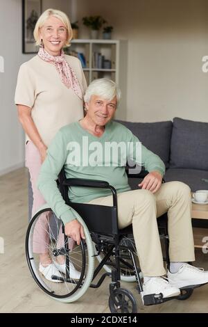 Porträt einer älteren Frau, die in der Nähe der Kamera lächelt Ihr behinderter Mann im Rollstuhl Stockfoto