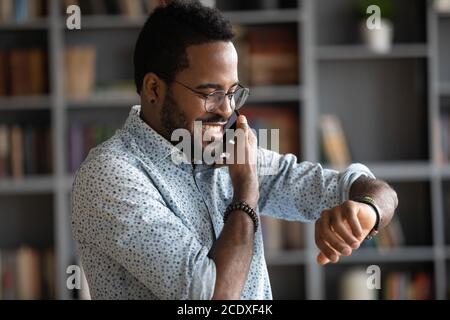 Lächelnder afroamerikanischer Mann, der die Zeit beim Telefonieren überprüft Stockfoto