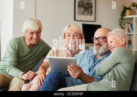 Eine Gruppe älterer Leute, die auf dem Sofa sitzen und etwas beobachten Auf einem digitalen Tablet zu Hause Stockfoto
