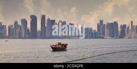 Doha Skyline von der corniche Promenade Sonnenuntergang Aufnahme zeigt Dhow Mit Qatar Flagge im arabischen Golf im Vordergrund und Wolken im Himmel im Hintergrund Stockfoto