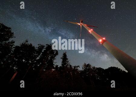 Industrielle Windturbine inmitten von Wald, nightshot mit Milchstraße und Sternenhimmel. Nachhaltige Energiewende. Stockfoto