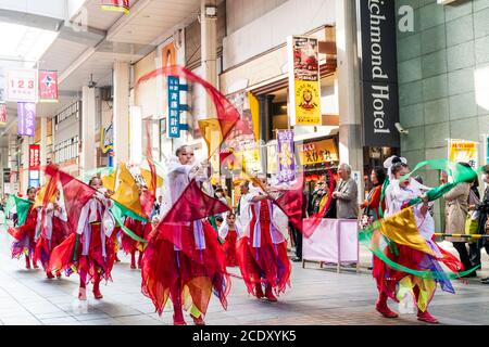 Japanisches Team von Kindern, 9-10 Jahre alt, yosakoi Tänzer tanzen in der Einkaufspassage und drehen um Kleidung am Ende der Stange. Bewegungsunschärfe. Stockfoto