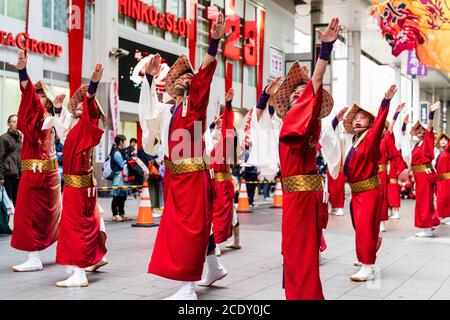 Japanisches Team von yosakoi-Tänzern, die Strohhüte und rote Happi-Mäntel tragen, tanzt während des Kyusyu Gassai Festivals in der Einkaufspassage Sun Road. Stockfoto