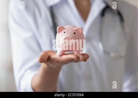 Nahaufnahme Frau trägt weißen Mantel, Arzt hält Sparschwein Stockfoto