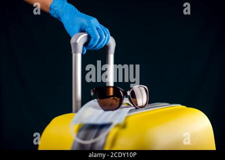 Gepäck mit medizinischer Gesichtsmaske. Hand in medizinischen Handschuhen Gepäck halten. Reise- und Coronavirus-Konzept. Studioaufnahme Stockfoto