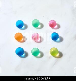 Quadratisches Muster aus hydrogelfarbenen Kugeln auf einem grauen Marmortisch. Stockfoto