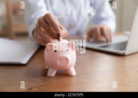 Nahaufnahme junge Frau Arzt Putting Münze in Sparschwein Stockfoto